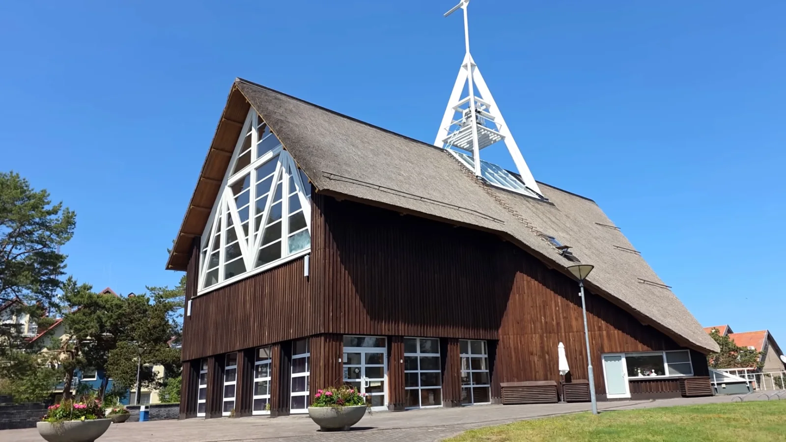 Wooden church with a thatched roof in Nida under a clear blue sky.
